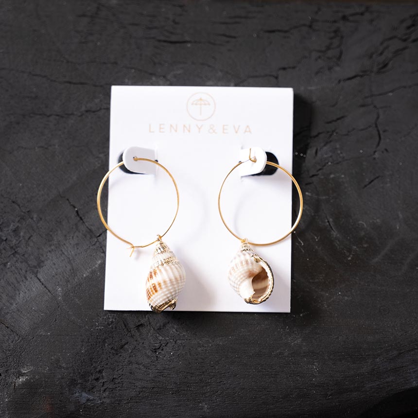 Top view of the Lenny & Eva white shell earrings against a rustic wood backdrop