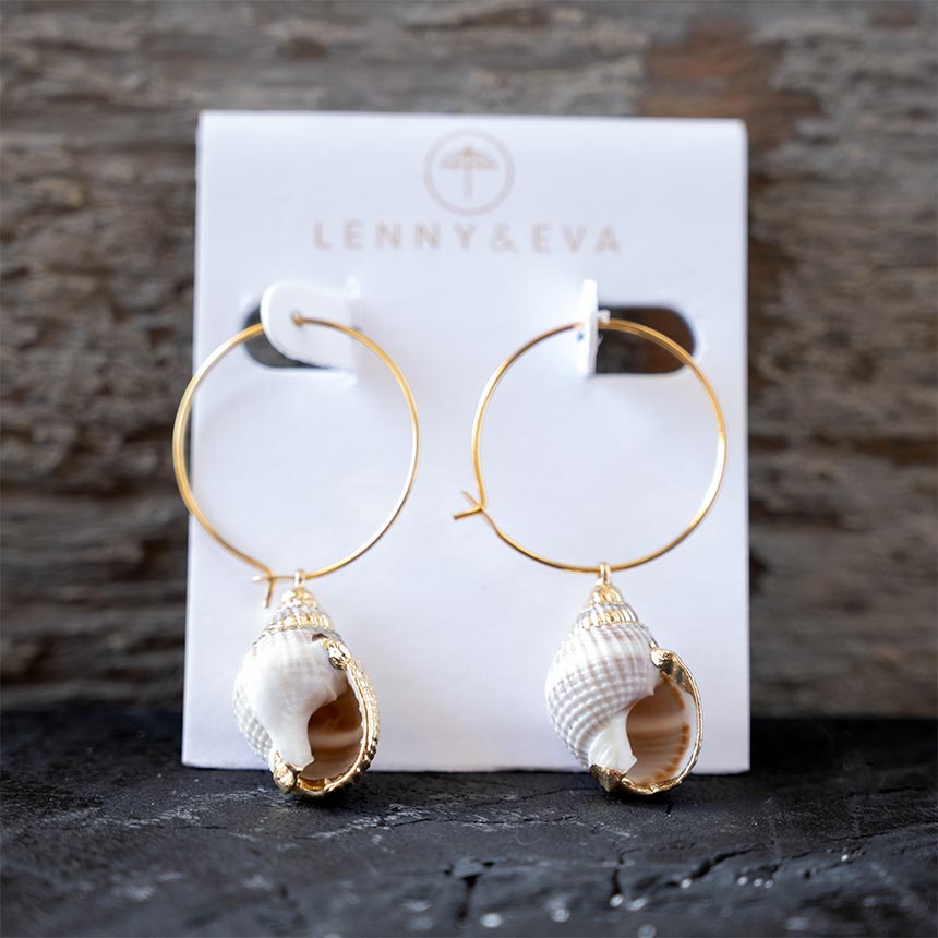Front view of the Lenny & Eva white shell earrings against a rustic wood backdrop