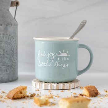 Left view of the Doe A Deer Find JOy in the Little Things mug with a spoon, biscotti and a rustic planter