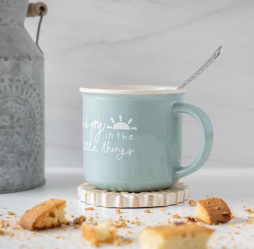 Left angle view of the Doe A Deer Find JOy in the Little Things mug with a spoon, biscotti and a rustic planter