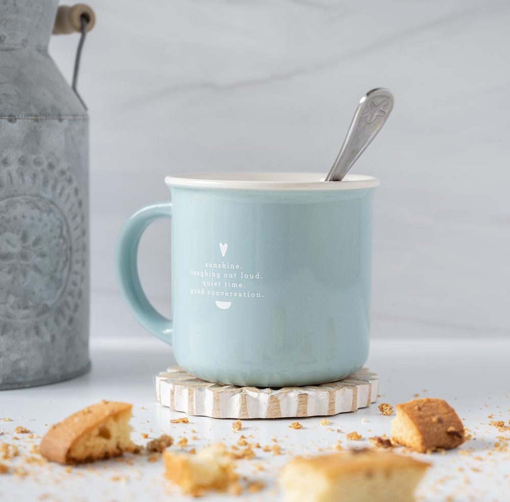 Right angle view of the Doe A Deer Find JOy in the Little Things mug with a spoon, biscotti and a rustic planter