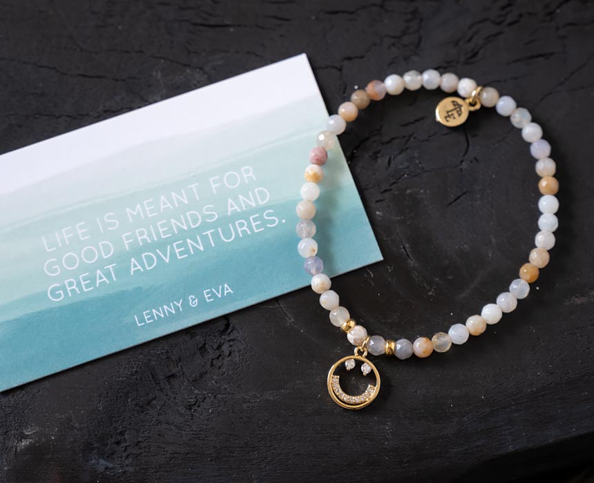 Top view of the Lenny & Eva Smiley Wanderlust bracelet with card on a piece of rustic wood