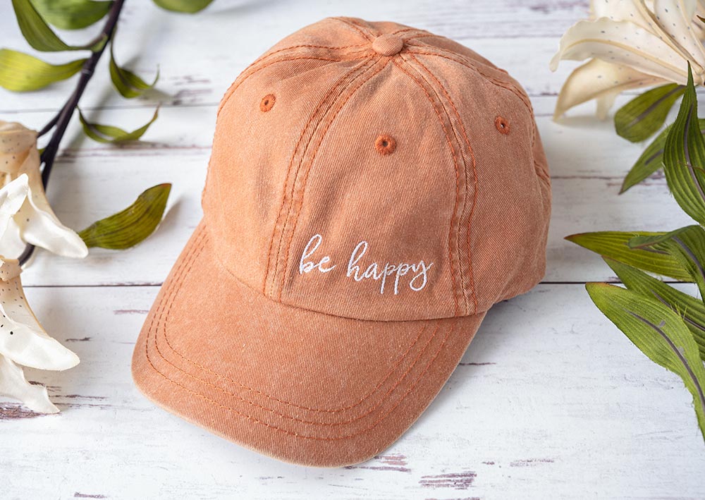 Women's Be Happy vintage hat on rustic wood backdrop with flowers