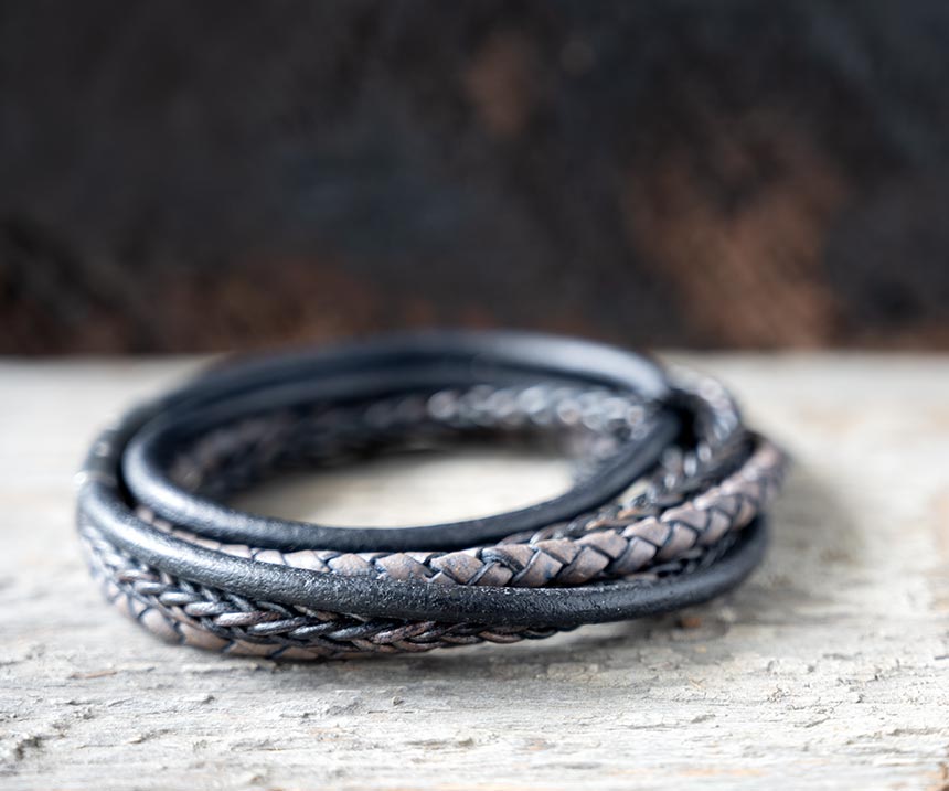 Left side view of the navy leather Bonacci bracelet by Steel & Barnett on a rustic piece of wood and backdrop
