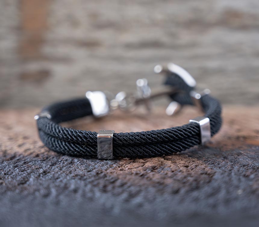 Back view of the Maris Sal Nautical Anchored New Haven bracelet in black resting on top of a piece of rustic wood