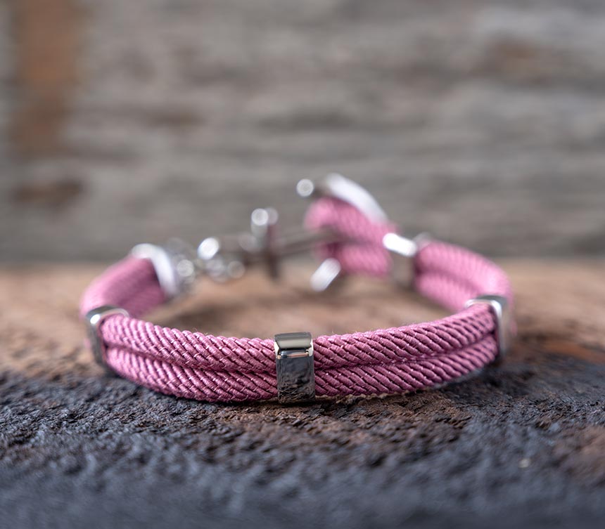 Back view of the Maris Sal Nautical Anchored New Haven bracelet in dusty pink resting on top of a piece of rustic wood