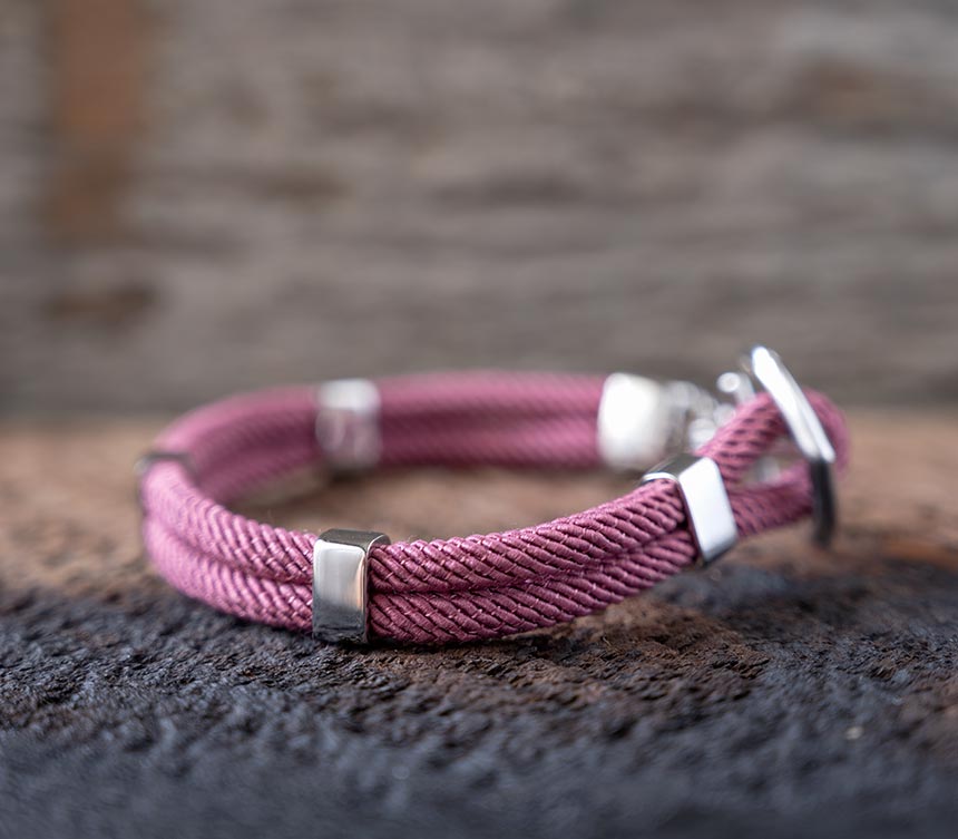 Right side view of the Maris Sal Nautical Anchored New Haven bracelet in dusty pink resting on top of a piece of rustic wood