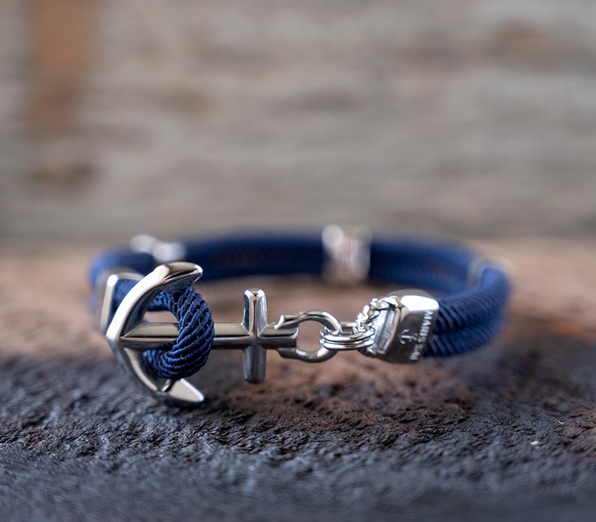 Front view of the Maris Sal Nautical Anchored New Haven bracelet in navy resting on top of a piece of rustic wood