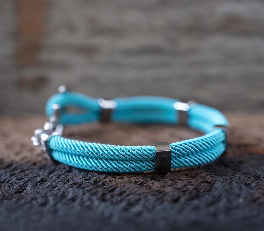 Left side view of the Maris Sal Nautical Anchored New Haven bracelet in turquoise resting on top of a piece of rustic wood