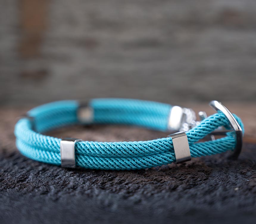 Right side view of the Maris Sal Nautical Anchored New Haven bracelet in turquoise resting on top of a piece of rustic wood