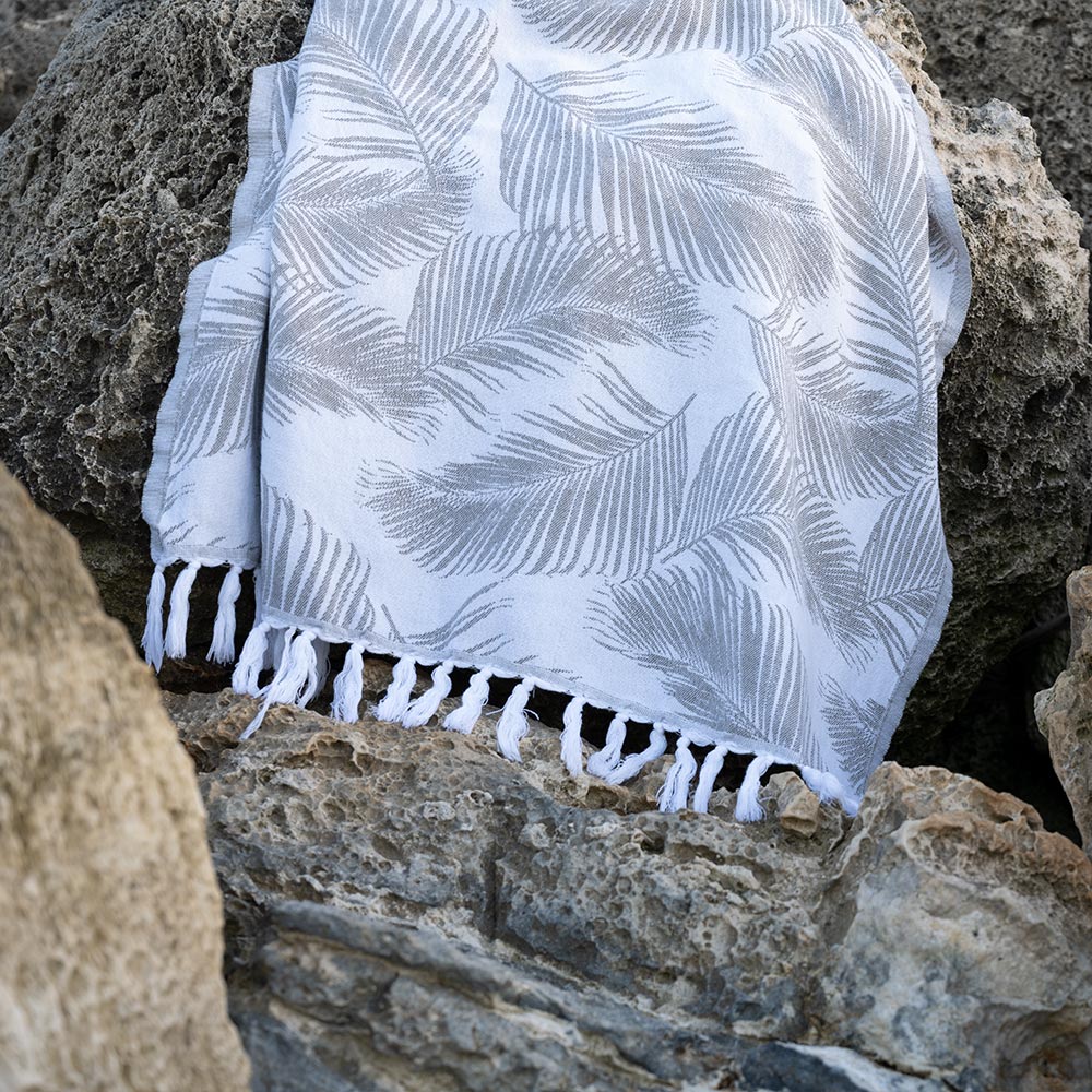 Olive Palms Turkish Towel by Case+Drift draped over rocks along a shoreline