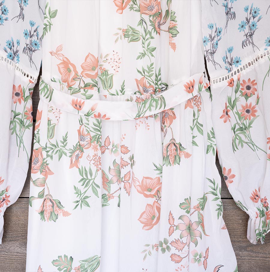 Closeup View of the Fabric of the Ranee’s Floral Off-Shoulder Dress Hanging Against a Wood Backdrop