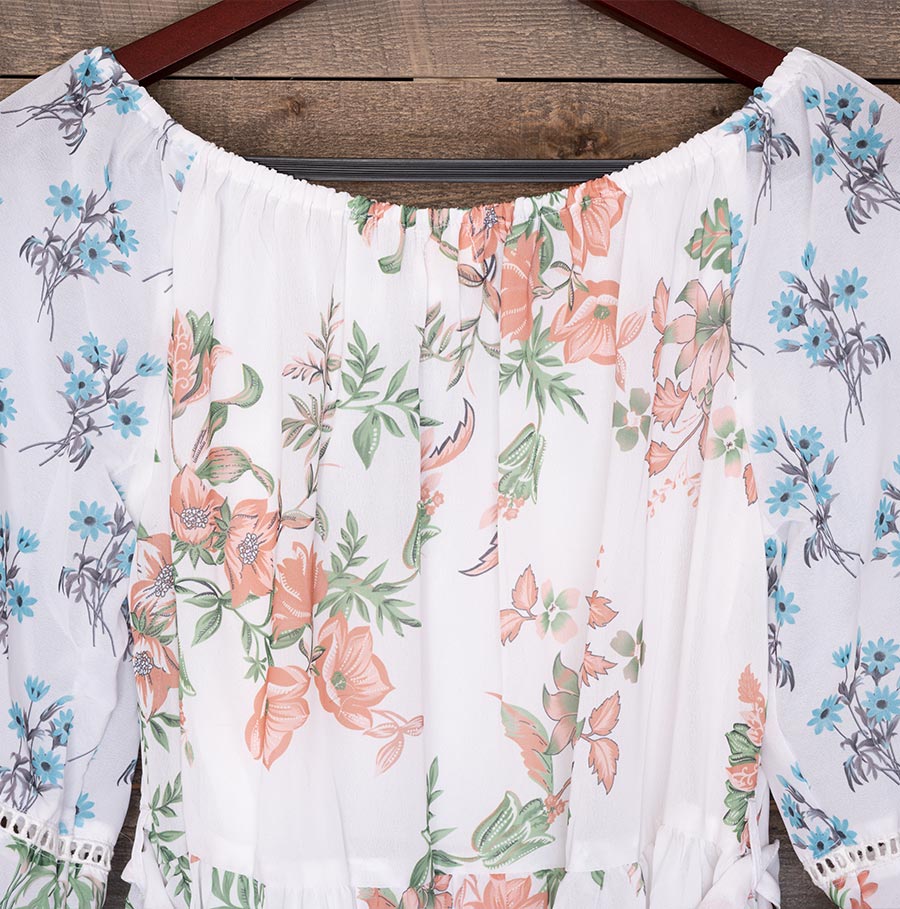 Back Closeup View of the Top of the Ranee’s Floral Off-Shoulder Dress Hanging Against a Wood Backdrop