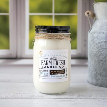 Front view of the Farm Fresh Candle Co Backwoods Candle on a wood top and in front of a window with trees