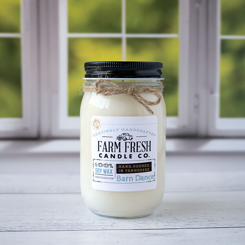The Barn Dance Fall scented soy candle by Farm Fresh Candle Co on a rustic wood top and window with blurred trees