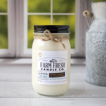 Front view of the Farm Fresh Candle Co Summer Farmhouse Candle on a wood top and in front of a window with trees