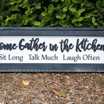 Come Gather in the Kitchen wood sign resting along shrubs