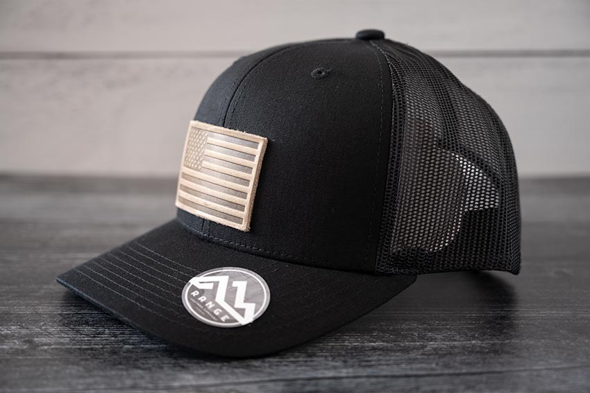Angled view of the RANGE Leather American Leather Patch Hat in black against a wooden backdrop