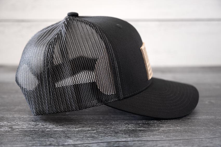 Right side view of the RANGE Leather American Leather Patch Hat in black against a wooden backdrop