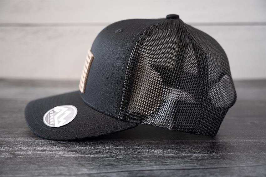 Side view of the RANGE Leather American Leather Patch Hat in black against a wooden backdrop