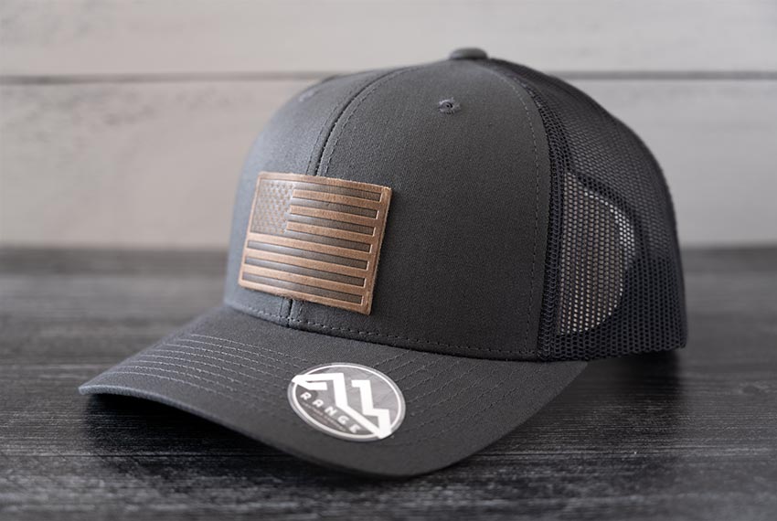 Angled view of the RANGE Leather American Leather Patch Hat in charcoal against a wooden backdrop