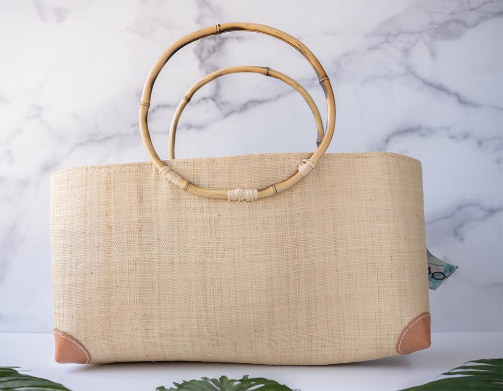 Side View of the Shebobo Bebe Straw Bag with Bamboo Handles withPalmnLeaves Laying in Front