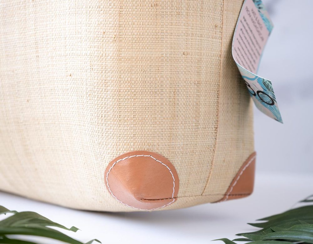 Lower Corner View of the Shebobo Bebe Straw Bag with Bamboo Handles with Palmn Leaves Laying in Front