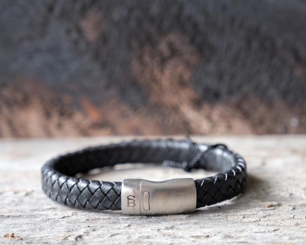 Front view of the Steel & Barnett Cornall bracelet in black on and against a rustic wooden backdrop