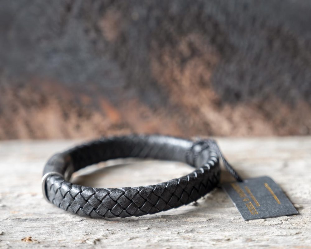 Left view of the Steel & Barnett Cornall bracelet in black on and against a rustic wooden backdrop