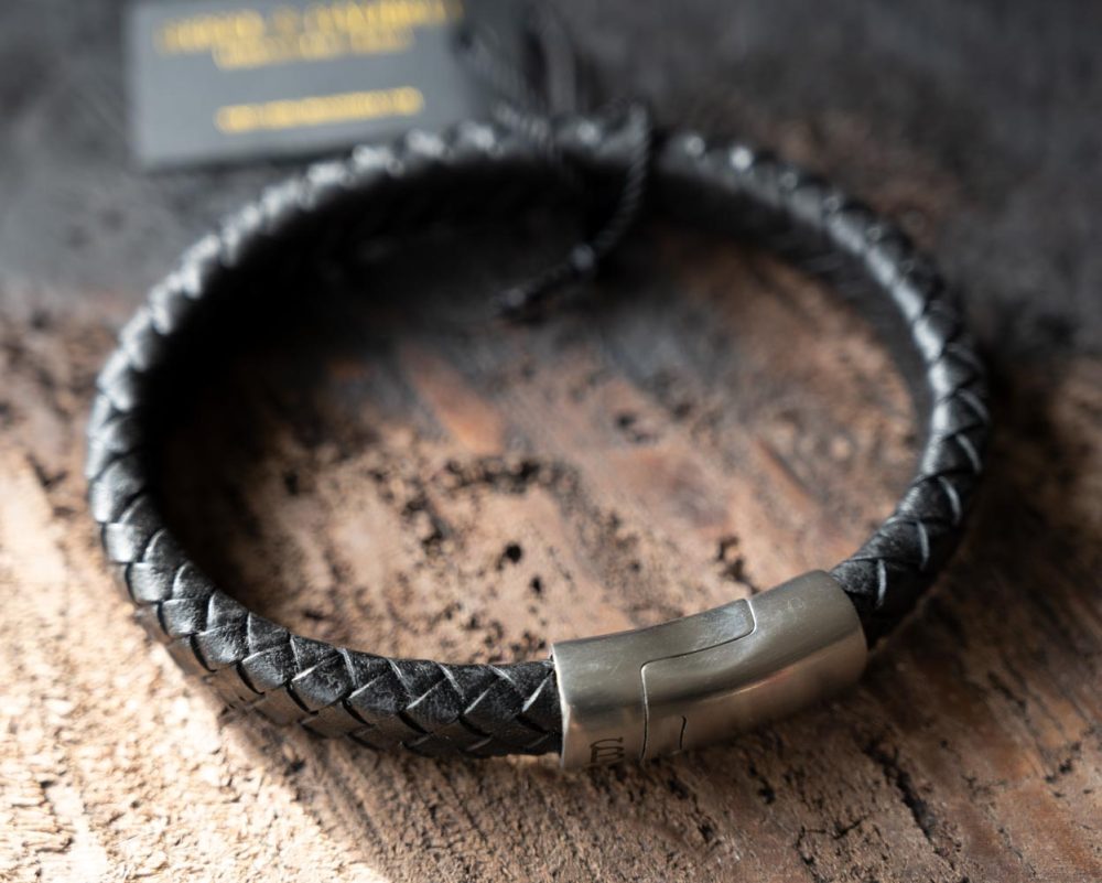Top view of the Steel & Barnett Cornall bracelet in black on and against a rustic wooden backdrop