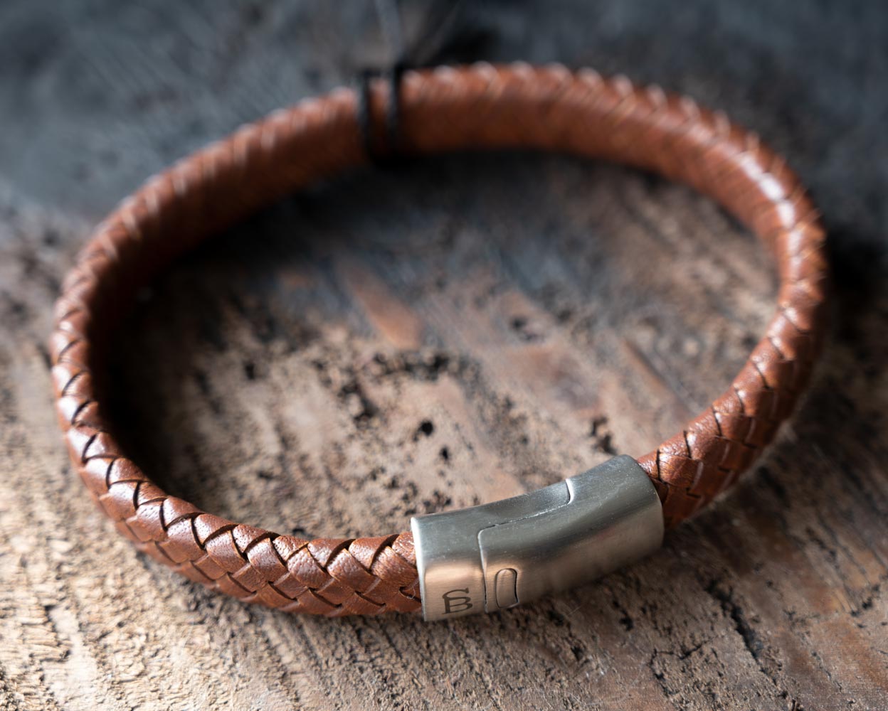 Top view of the Steel & Barnett Cornall bracelet in caramel on and against a rustic wooden backdrop
