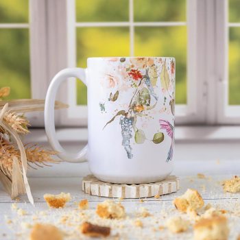 Right view of the Florae & Snow Hummingbird coffee mug against a window and on a coaster and wood top