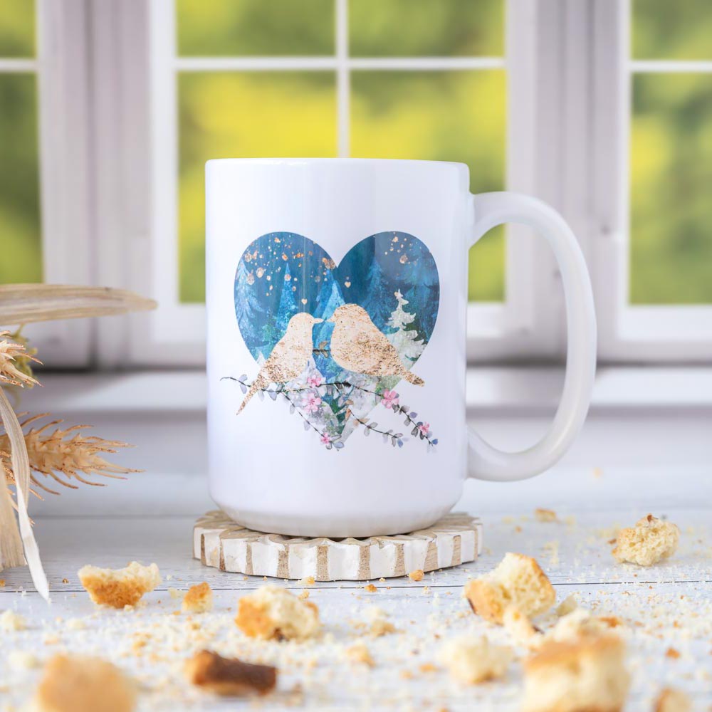 Left view of the Florae & Snow Lovebirds Mug Night series of two lovebirds in front of a heart on th emug on wooden top layered with biscotti and in front of a window