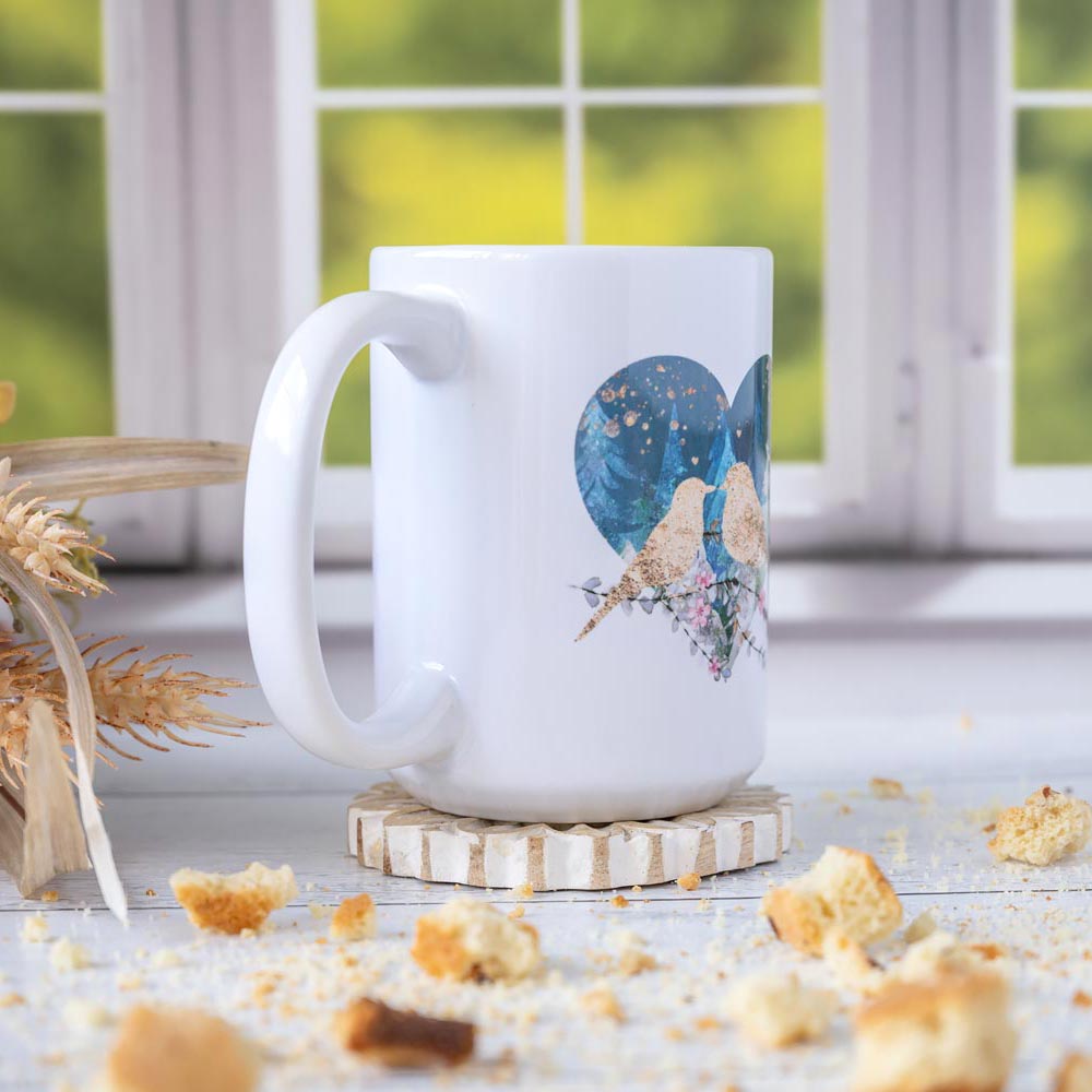 Right angle of the Florae & Snow Lovebirds Night Mug series of two lovebirds in front of a heart on th emug on wooden top layered with biscotti and in front of a window