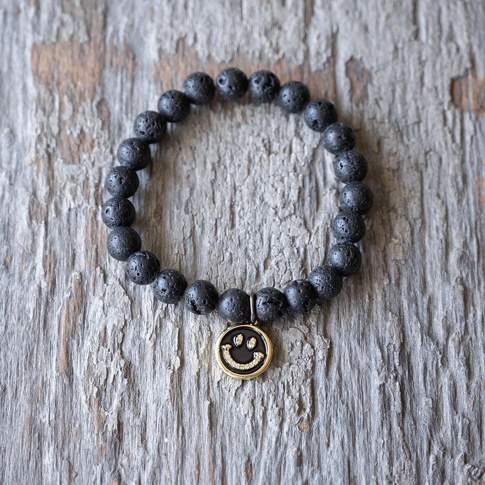 Front view of the Smiley Face Oil Lava Beads Bracelet by VB&CO Designs on rustic wood backdrop