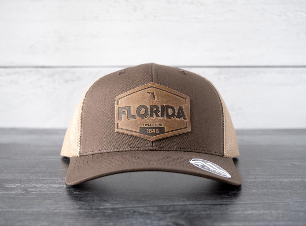 Front view of the RANGE Leather Florida Established hat in brown & khaki on and against a rustic wood backdrop