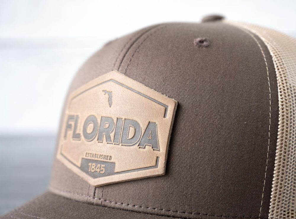 Closeup view of the RANGE Leather Florida Established hat in brown & khaki on and against a rustic wood backdrop
