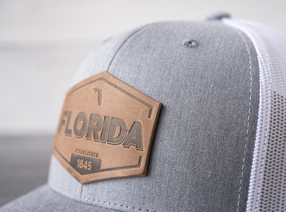 Closeup view of the RANGE Leather Florida Established hat in heather gray & white on and against a rustic wood backdrop