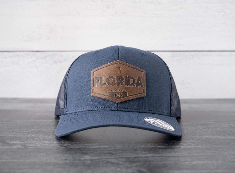 Front view of the RANGE Leather Florida Established hat in navy on and against a rustic wood backdrop