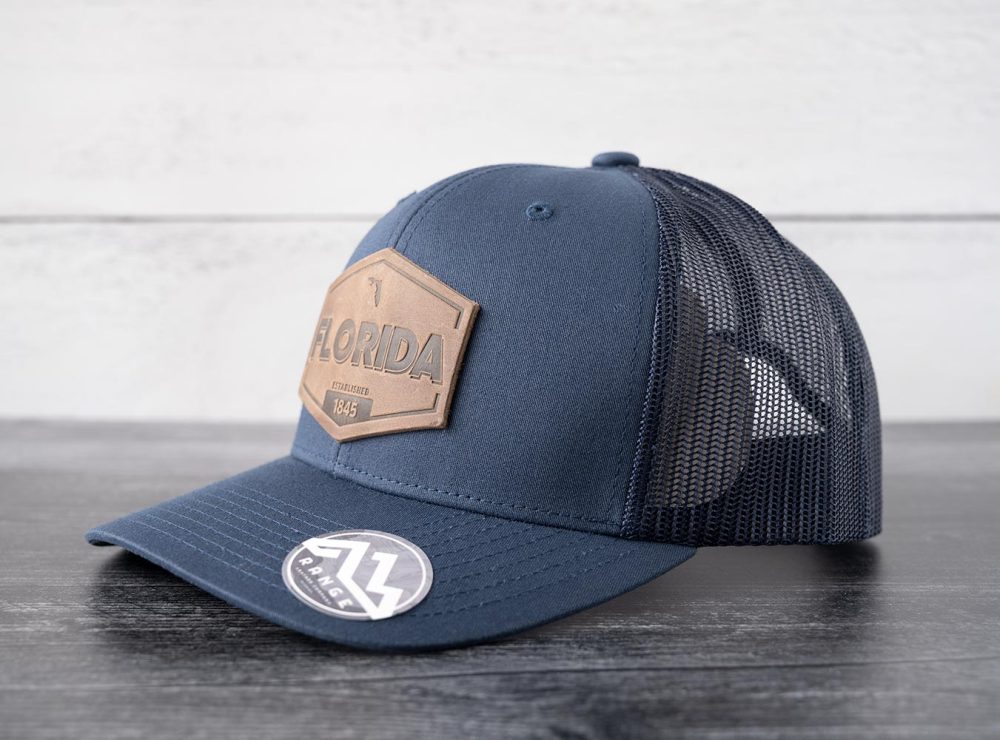 Left side view of the RANGE Leather Florida Established hat in navy on and against a rustic wood backdrop