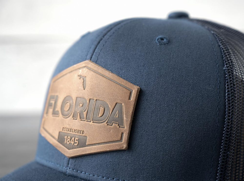 Closeup view of the RANGE Leather Florida Established hat in navy on and against a rustic wood backdrop