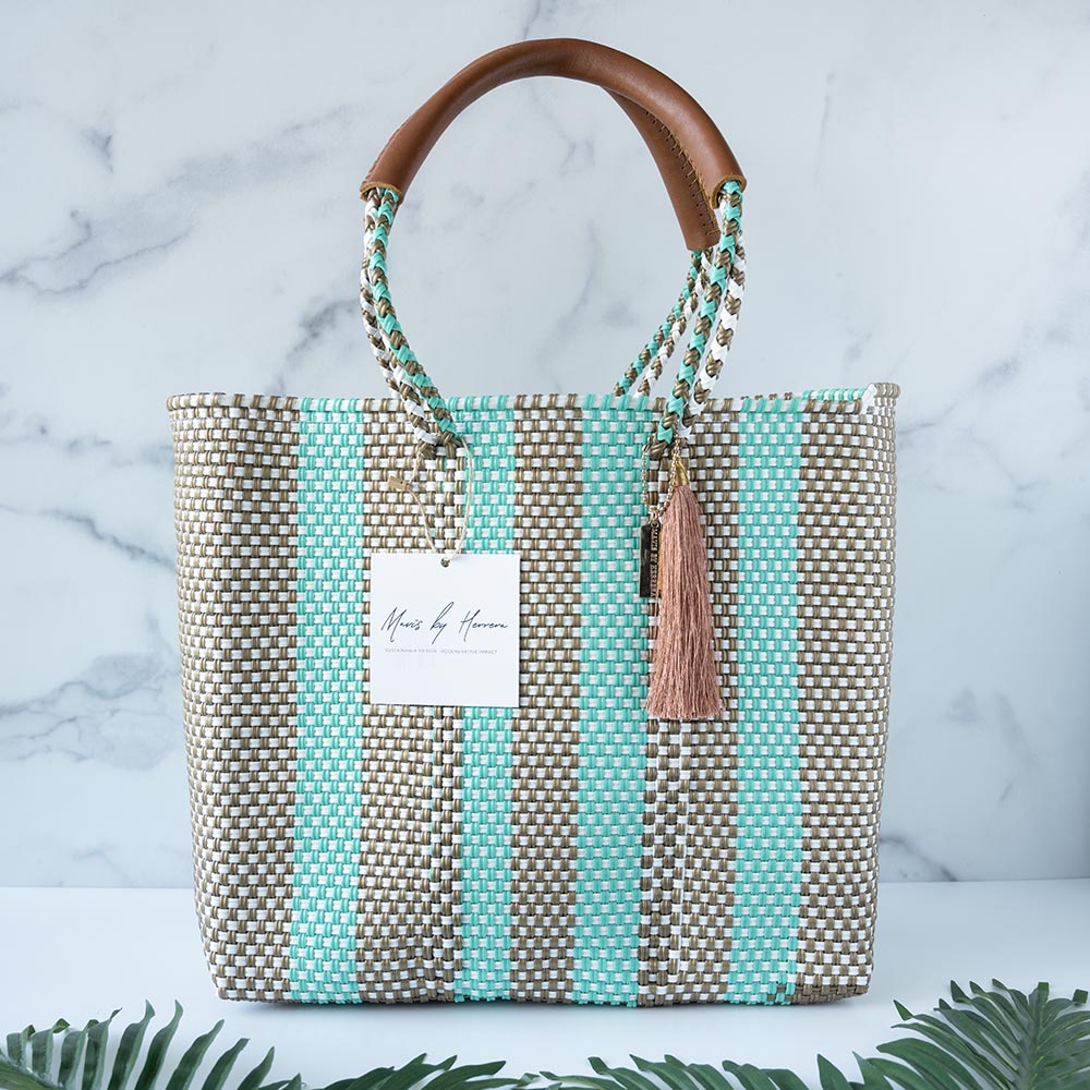 Front view of the Mavis by Herrera Hannah Resort Tote bag in Bora Bora against a white and marble background with palm leaves in front of the bag
