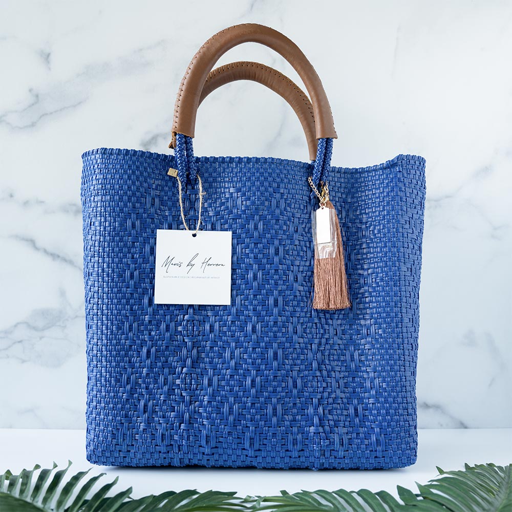Front view of the Mavis by Herrera Hannah Resort Tote bag in Ocean Blue against a white and marble background with palm leaves in front of the bag