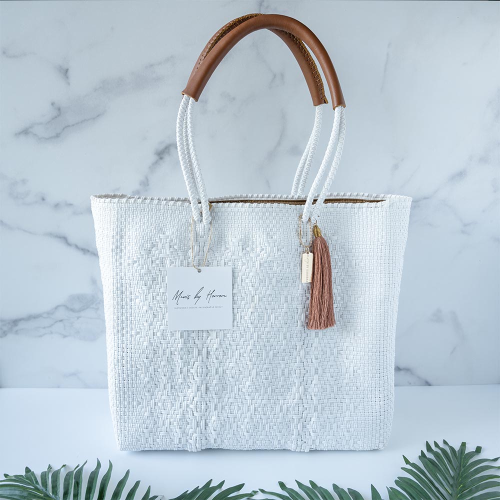 Front view of the Mavis by Herrera Hannah Resort Tote bag in Pearl White against a white and marble background with palm leaves in front of the bag