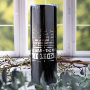 Emma K Designs Dad, the Myth, the Legend Camo American Flag Saying Skinny 20 oz. tumbler in th ecolor black on rustic backdrop with window and flowers