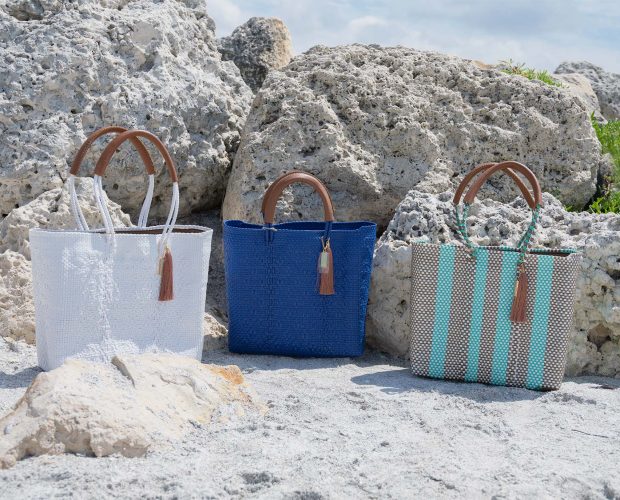 The Hannah Resort Tote Bag Collection by Mavis by Herrera alongside rocks on a sandy beach in Florida