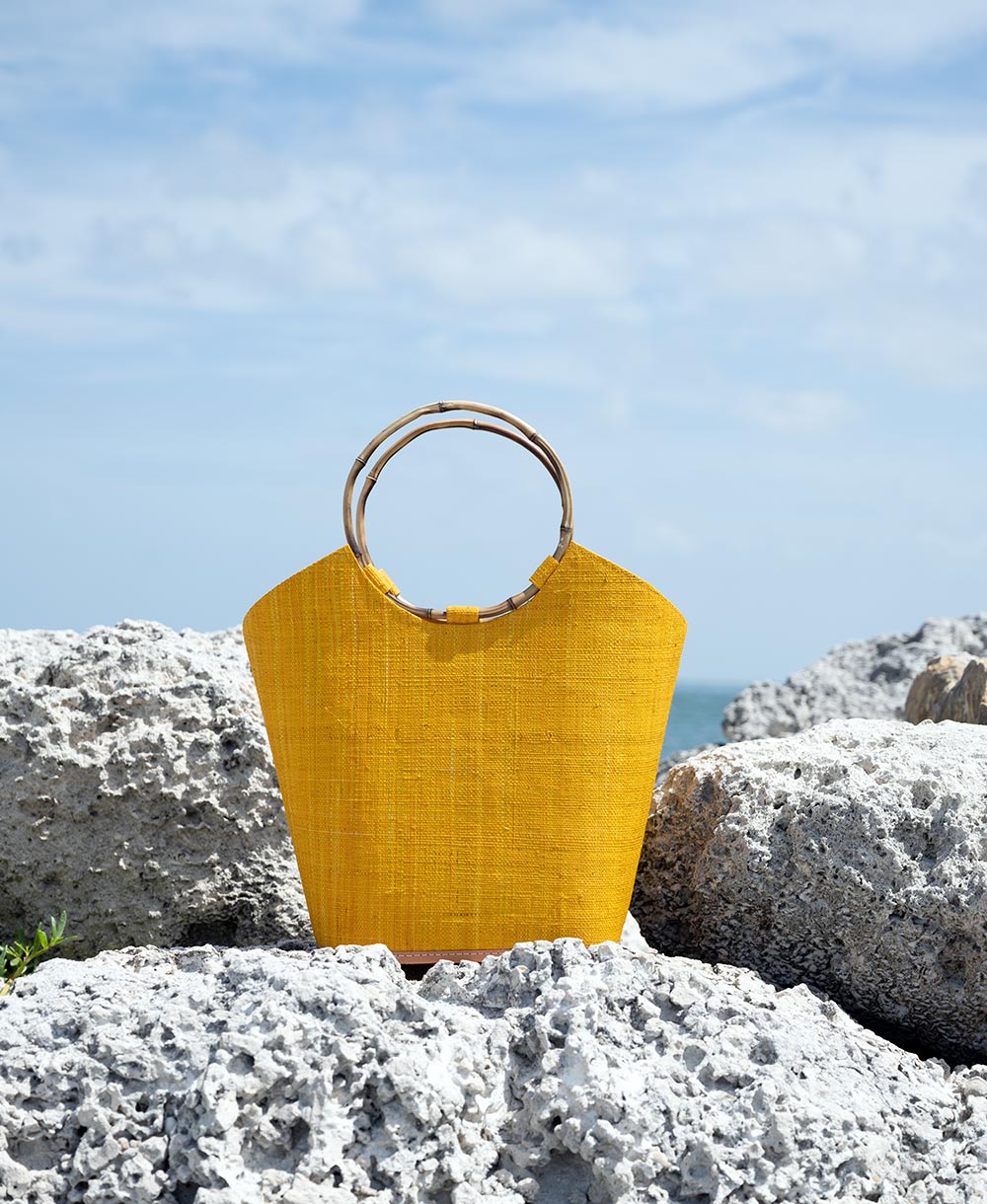 Back view of the Shebobo Carmen Straw Bucket Basket bag in saffron on the rocks at the beach