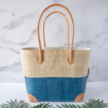 Front view of the Shebobo Trinidad Two Tone Tote Bag in turquoise against a clean white and marble background with palm leaves in front
