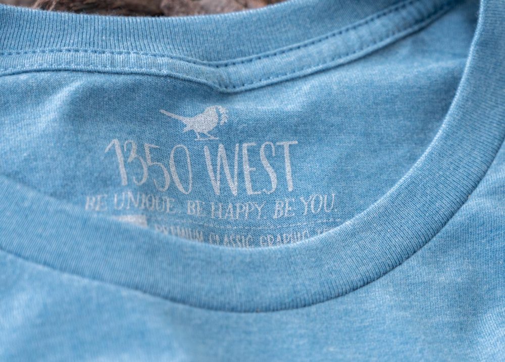 Closeup of the Collar and Inside Branded Tagging of the Salty. Sandy. Happy women's graphic tee on a wooden boardwalk background with nautical and beach accents around it