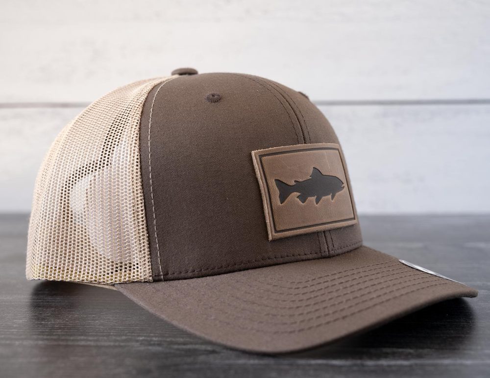 Left angled view of the RANGE Leather Trout hat in the color brown & khaki against a white and black rustic wood background